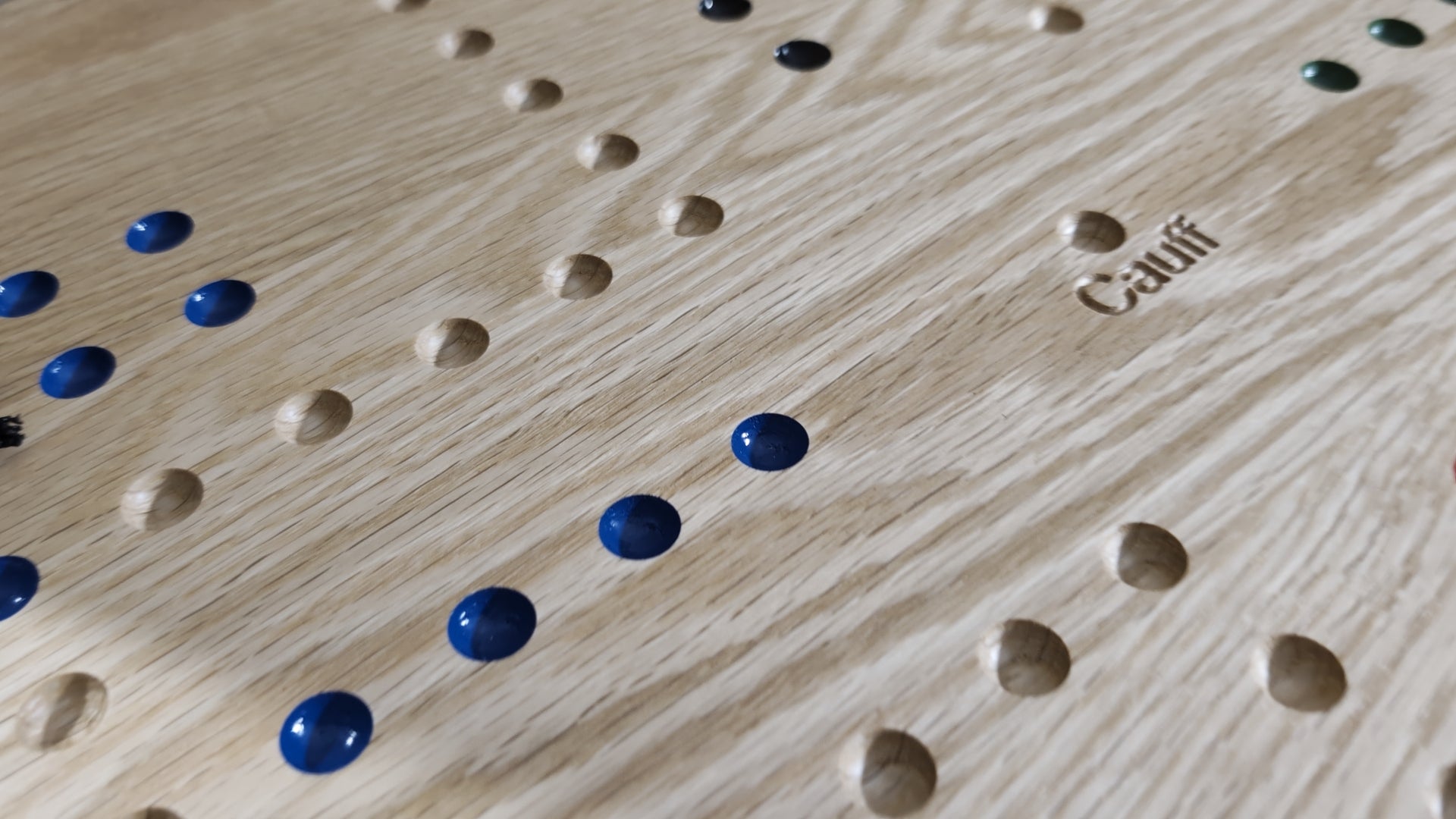 Close-up of a handcrafted oak CAUFF marble board with blue and neutral game marbles in routed playing holes.